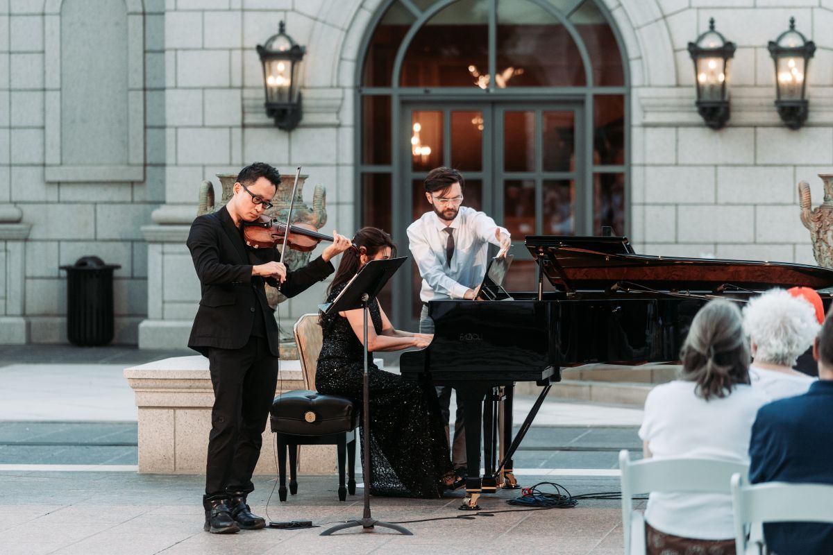 Musicians playing a violin, piano, and cello for a crowd