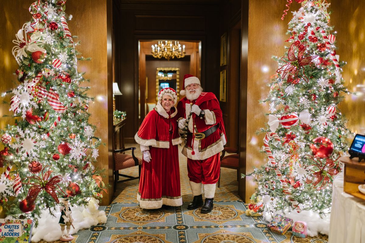 Santa and Mrs. Clause standing in between two Christmas trees