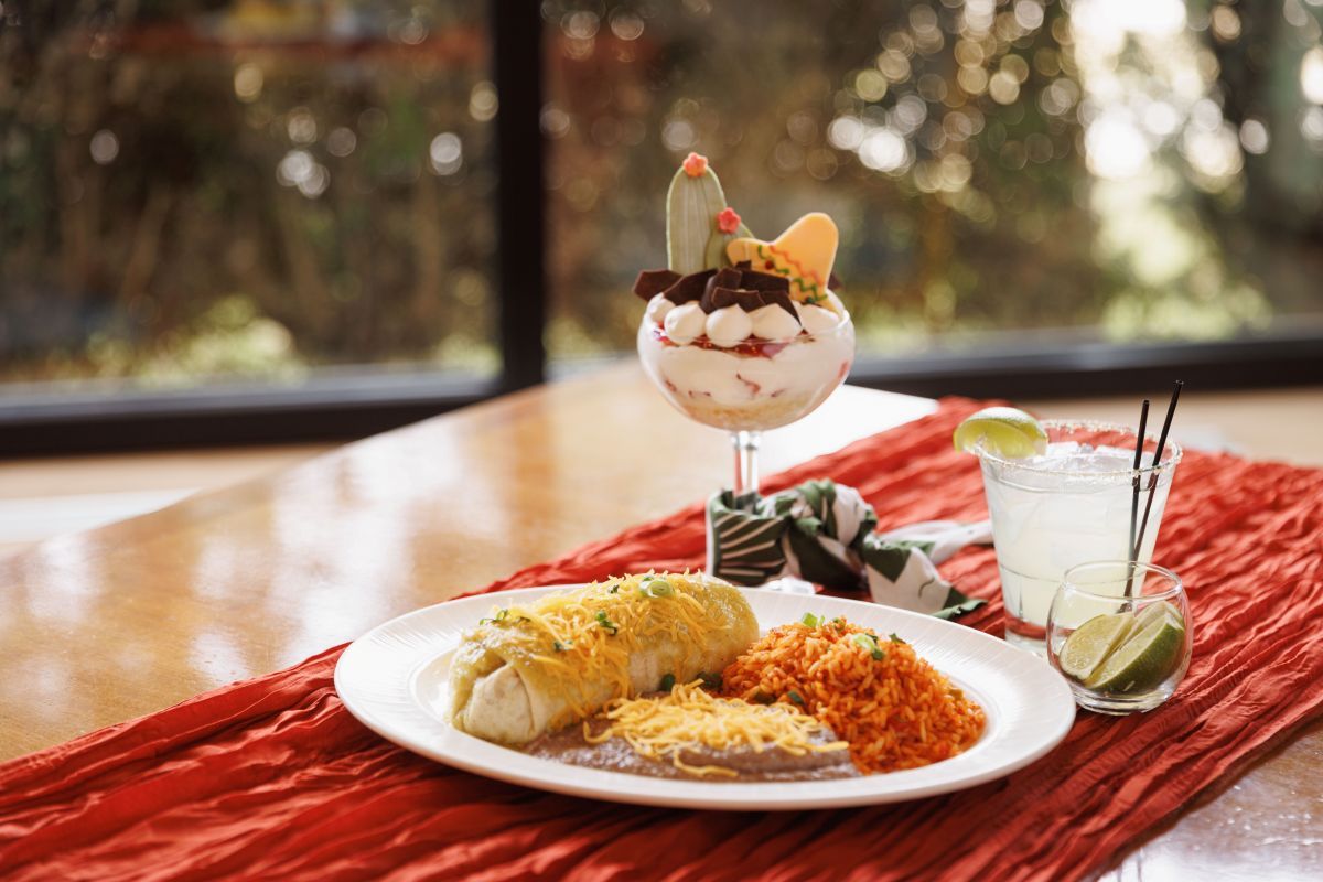 Plate with a burrito, rice, and refried beans alongside a margarita and dessert