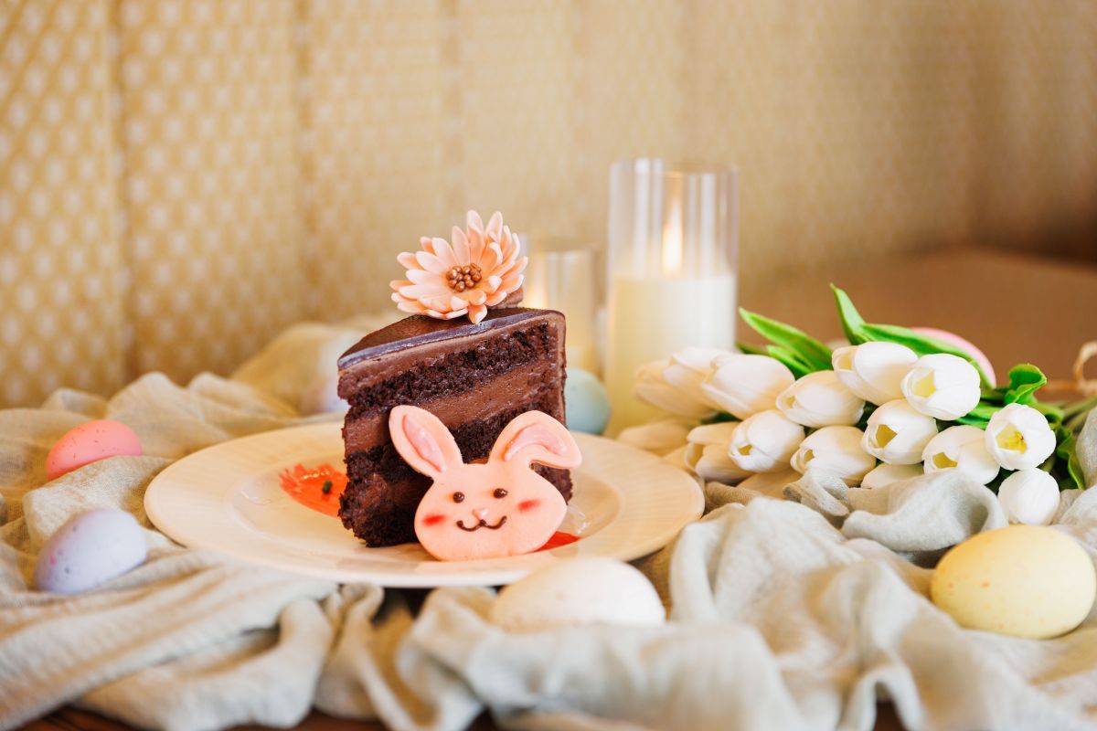 Piece of chocolate cake on a plate with a pink bunny head on a table with tulips