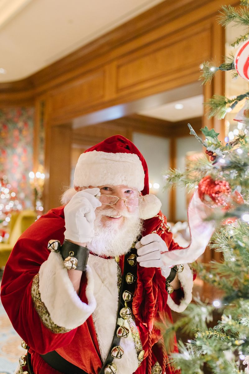 Santa standing in front of a Christmas tree touching his glasses